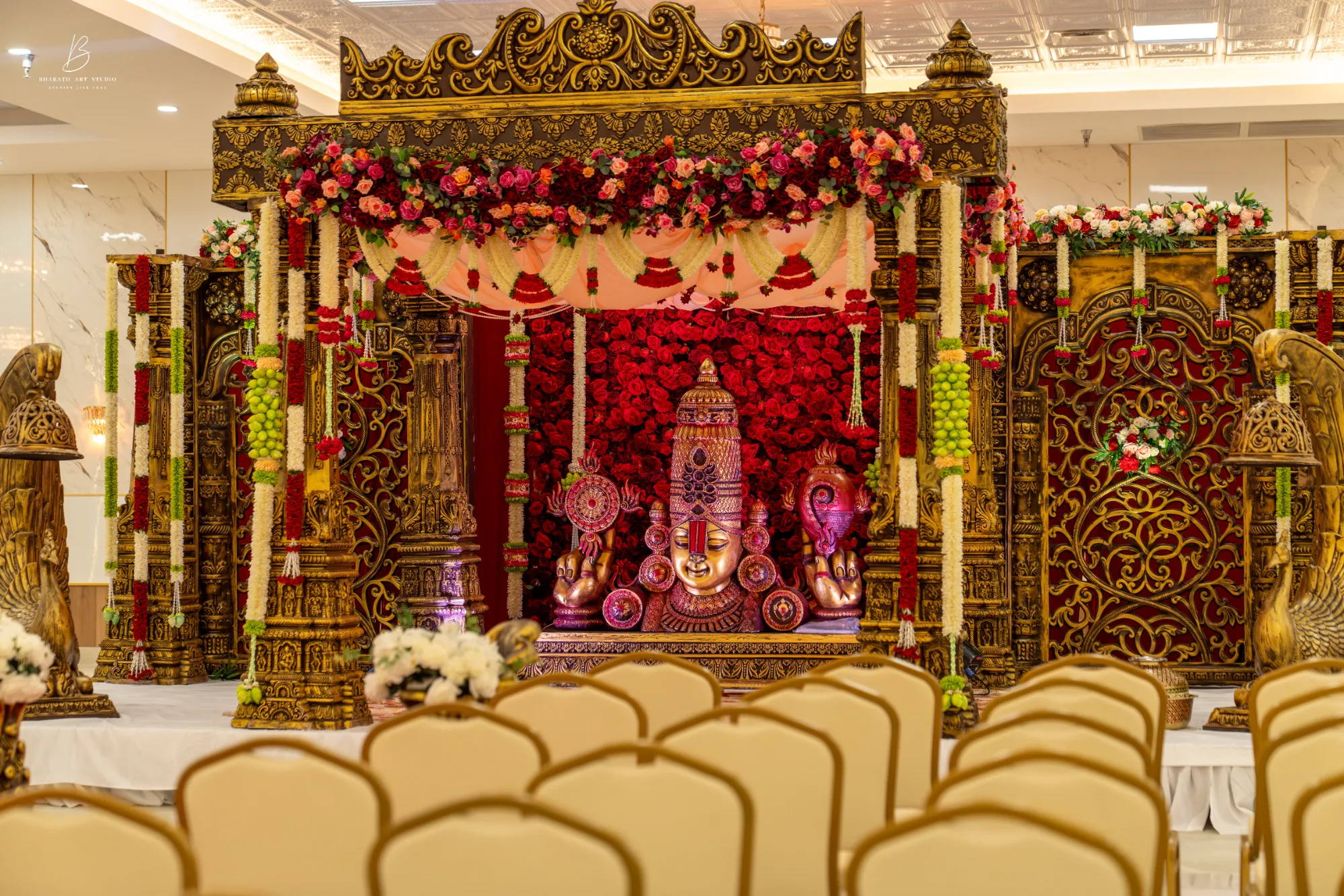 Carved golden mandap with a red rose backdrop and deity centerpiece at Triveni Banquet near Dulles