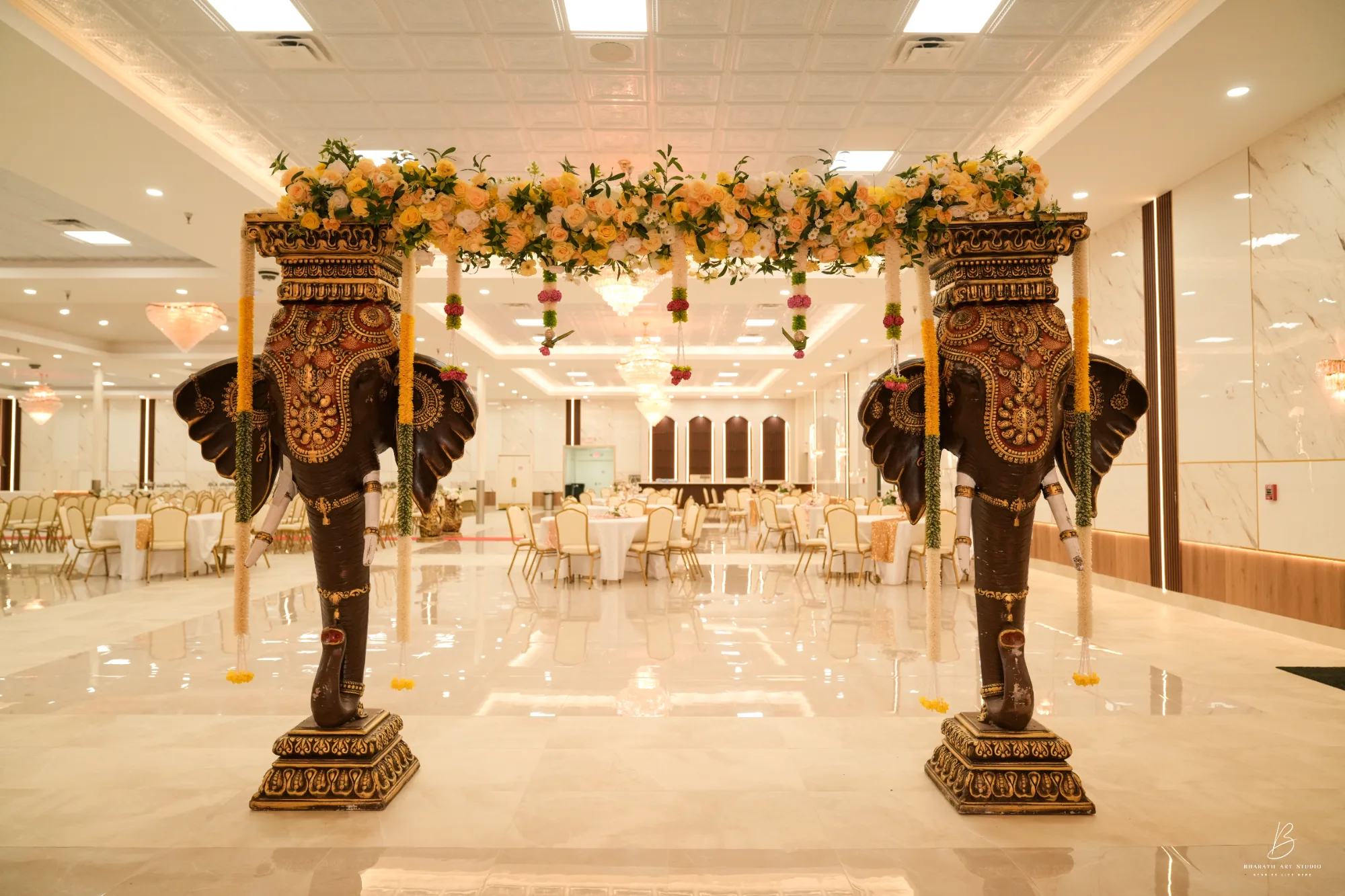 South Asian wedding mandap with carved elephant columns and a yellow floral canopy in Triveni's hall, South Riding, Loudoun County